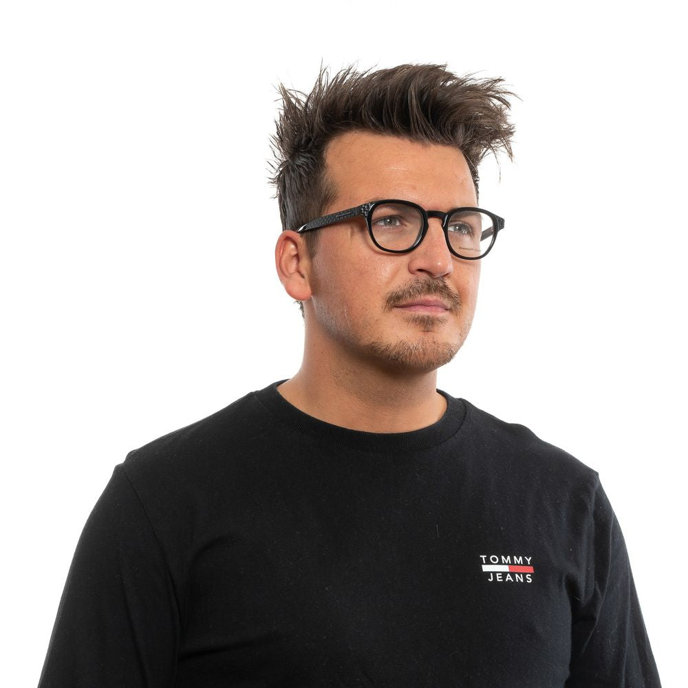 A man with spiky brown hair, light facial hair, and black round Ermenegildo Zegna plastic frames is wearing a black Tommy Jeans shirt. He is looking slightly to the right against a plain white background.