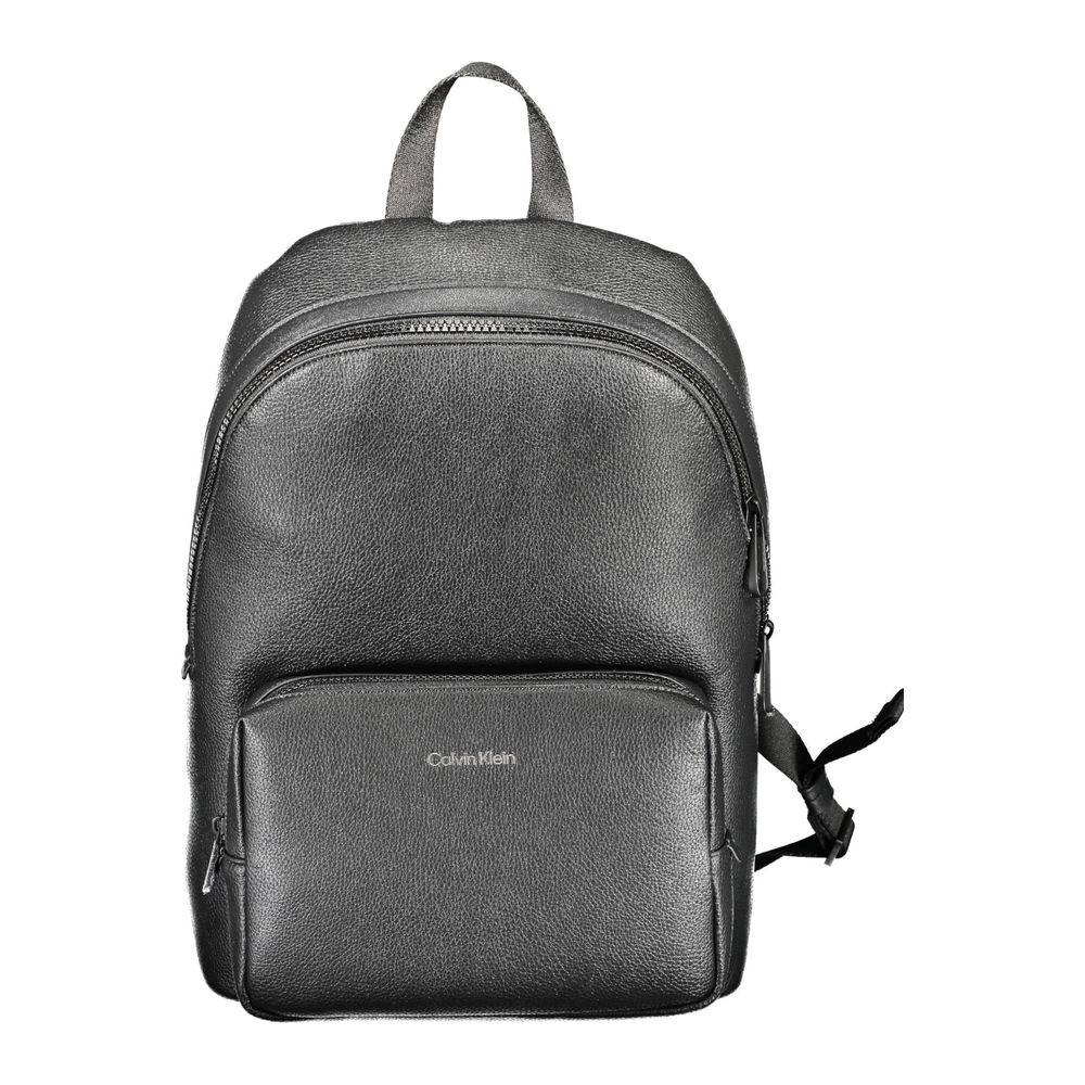 The Calvin Klein Nero Poliuretano Men Backpack features black polyurethane, a recycled polyester lining, front zippered pocket, adjustable straps, top handle, and a silver logo on the front. Shown against a white background.