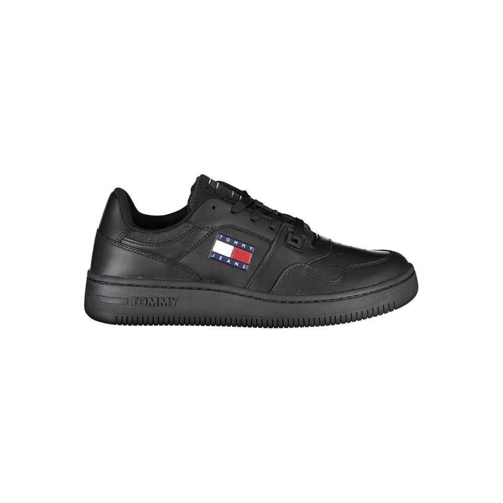 The Tommy Hilfiger Black Leather Women Sneaker is a low-top, lace-up shoe with an all-black sole and upper, featuring the Tommy Jeans logo and flag in red, white, and blue, plus “TOMMY” embossed on the heel.